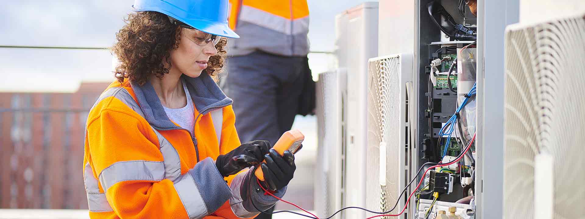 Une technicienne procède au diagnostic d’un système de climatisation sur le toit d’un édifice.