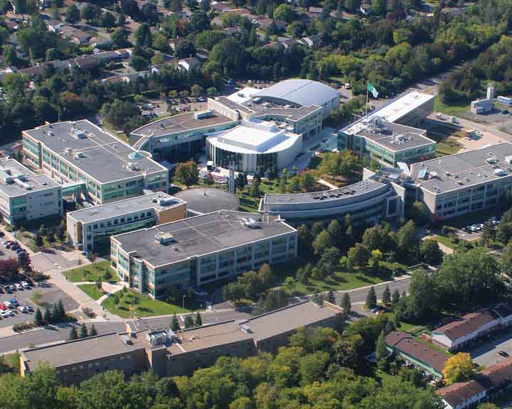 Vue aérienne, de La Cité, un campus aux bâtiments modernes, entourés d'arbres et de zones résidentielles. Les bâtiments, aux grandes fenêtres et aux styles architecturaux variés, sont reliés par des allées et des parkings.