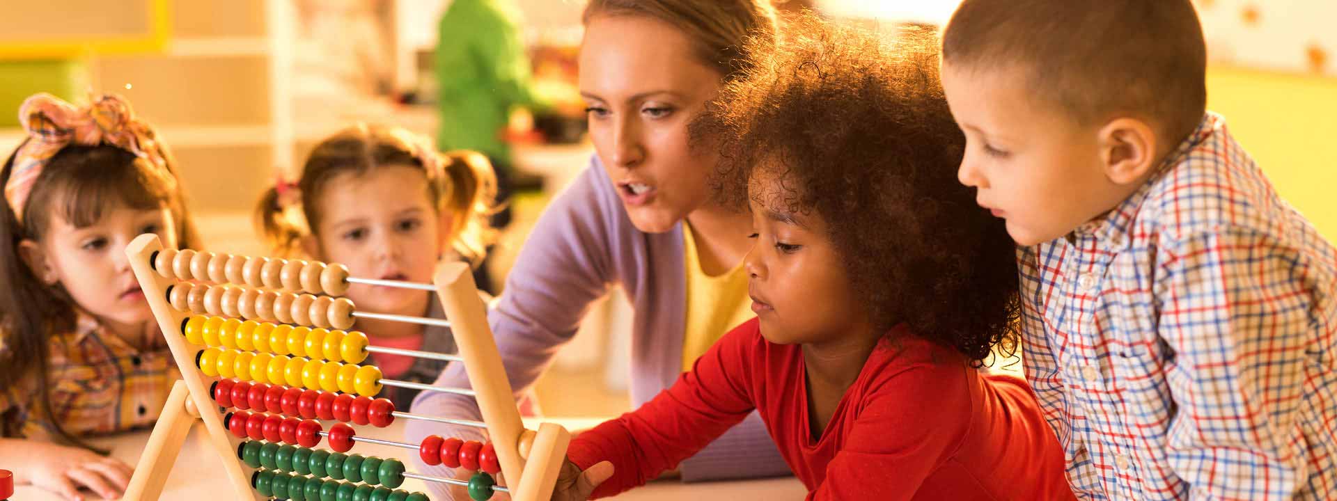 Une éducatrice dirige une activité avec trois enfants prenant place autour d'une table.