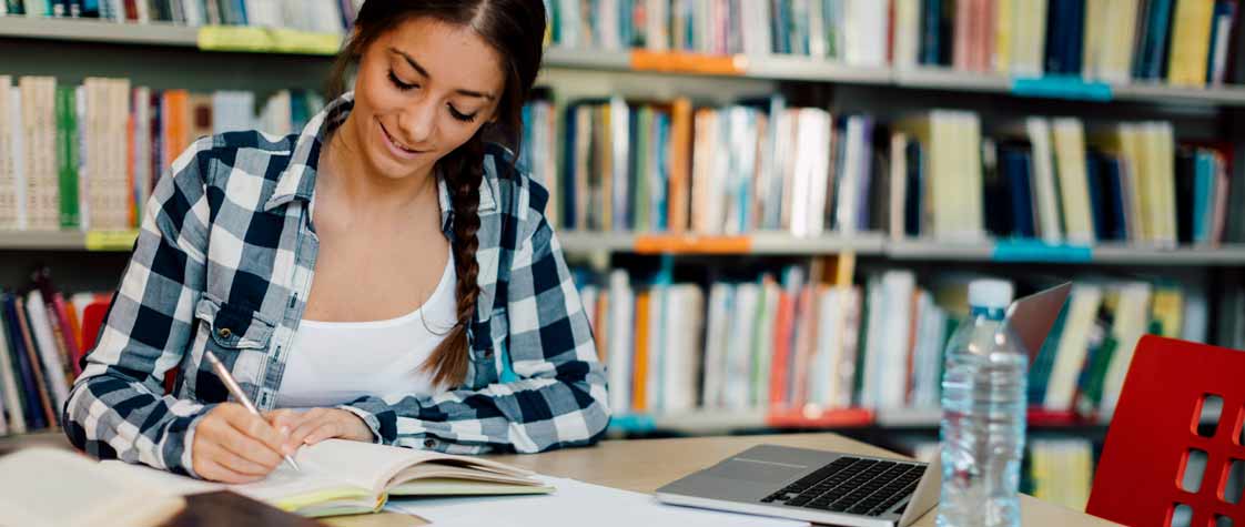 Étudiante assise, écrite dans un cahier dans une bibliothèque