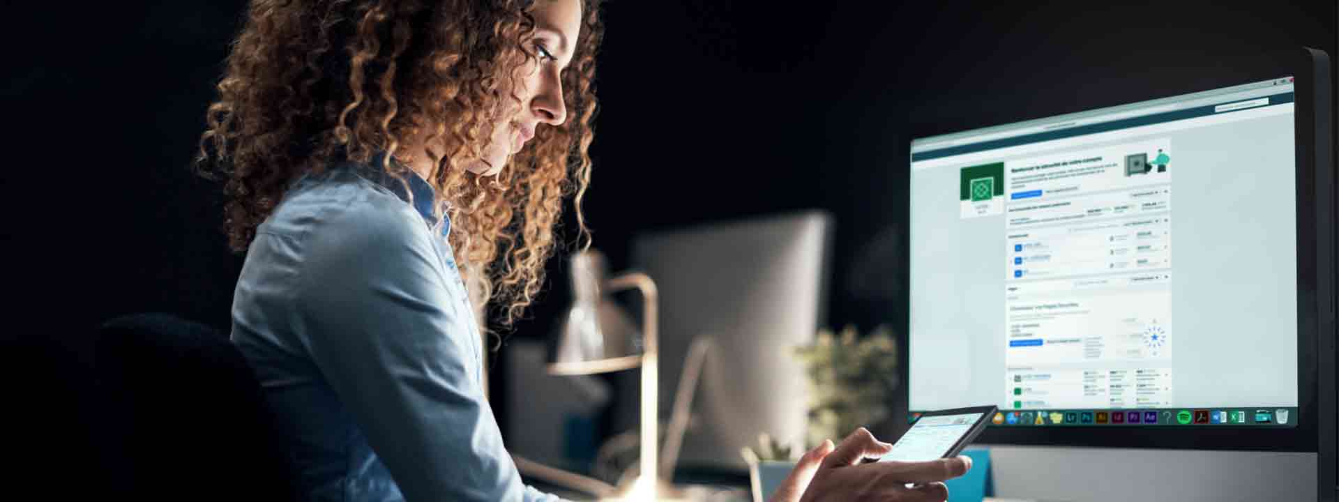 Une étudiante est assise à un bureau devant un ordinateur et un téléphone intelligent.