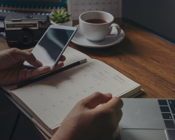 Personne qui écrit dans un agenda en consultant un mobile