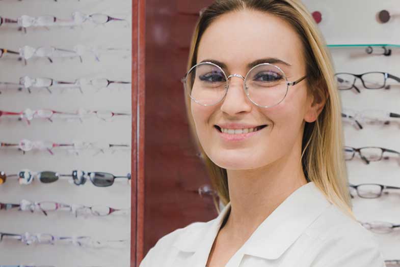 Opticienne devant des lunettes et regardant la caméra en souriant