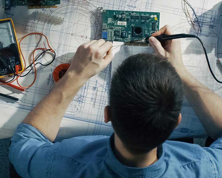 VUn étudiant installé à une table de travail utilise des équipements pour travailler sur des composants d'appareils électroniques.