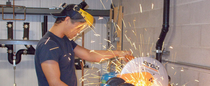 Un apprenti plombier du programme d'apprentissage PLOMBIER, coupe un tuyau dans l'atelier principal de plomberie à Orléans.