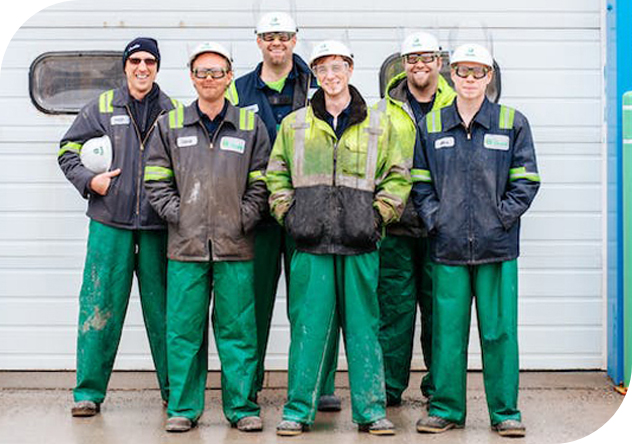 Équipe de travailleurs portant des lunettes de sécurité et des équipements de protection, devant un site industriel.