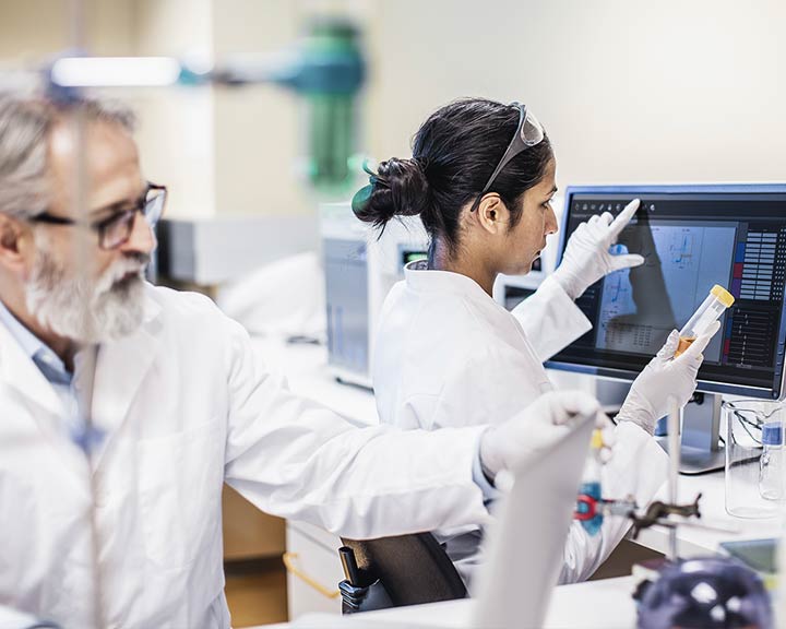 Deux scientifiques en laboratoire analysant des données à l’écran et un échantillon en tube.