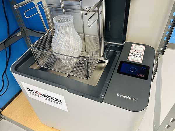 Machine Formlabs avec un objet imprimé en 3D translucide en forme de vase dans un panier métallique.