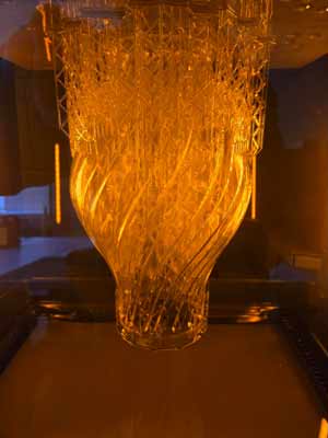 Vase translucide imprimé en résine, encore attaché à ses supports d'impression.