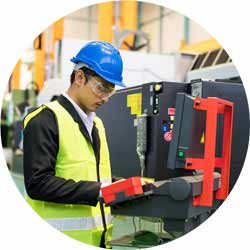 Worker with hardhat and protection glasses command computer to produce products by automate robot machines in factory workshop