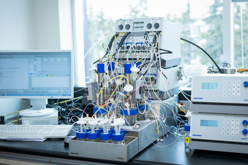 Laboratoire avec bioreacteur complexe, écrans et unités de contrôle, ambiance propre et professionnelle.