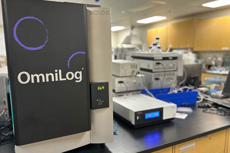 Laboratoire avec système OmniLog au premier plan, autres appareils et câbles en arrière-plan, environnement propre et bien éclairé.