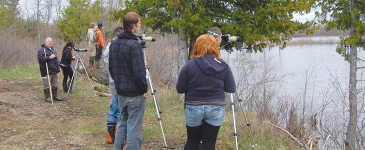 Des étudiants accompagnés d'un professeur observent la berge à l'aide de lunettes d'approche, programme Pratiques en environnement forestier, La Cité.