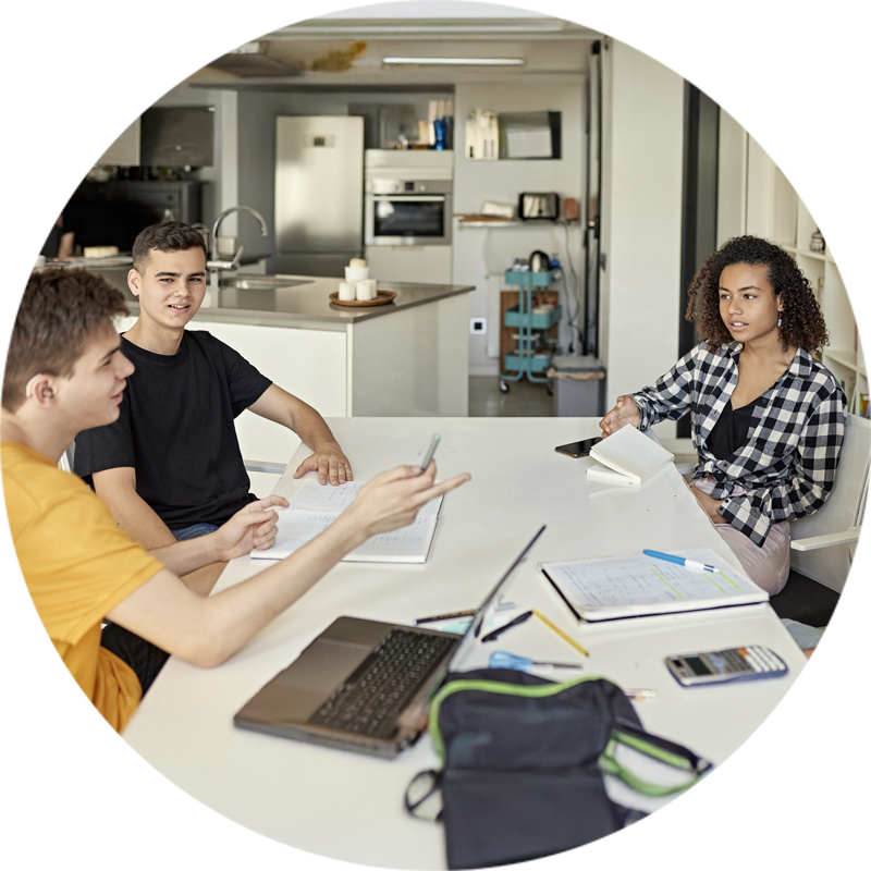 Jeunes travaillant ensemble sur un projet ou une session d’étude, autour d’une table remplie de cahiers, ordinateurs et fournitures, dans un espace intérieur lumineux et moderne.