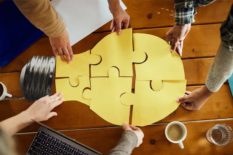 Vue aérienne d'une équipe créative méconnaissable en pleine collaboration, réalisant des puzzles en bulles lumineuses dans un bureau décontracté.