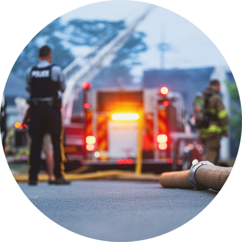 Scène d’urgence avec un camion de pompiers en intervention, un tuyau d’incendie au premier plan et des intervenants en action, capturant la dynamique et l’urgence d’un incendie.