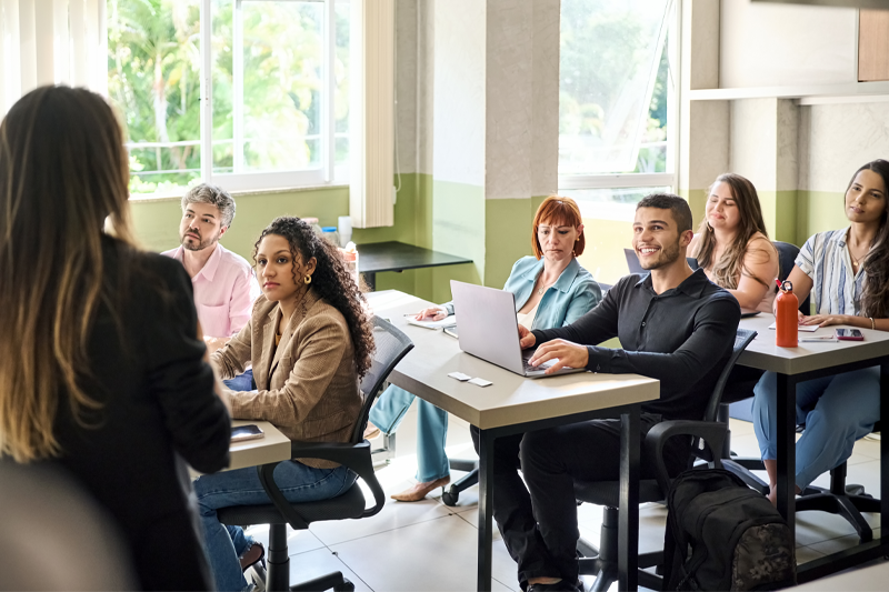 Groupe d'étudiants adultes écoutant attentivement une conférencière en classe.