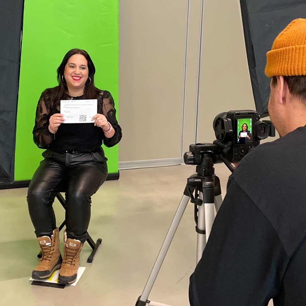  Femme assise tenant un document devant un fond vert pendant qu’un photographe la prend en photo.
