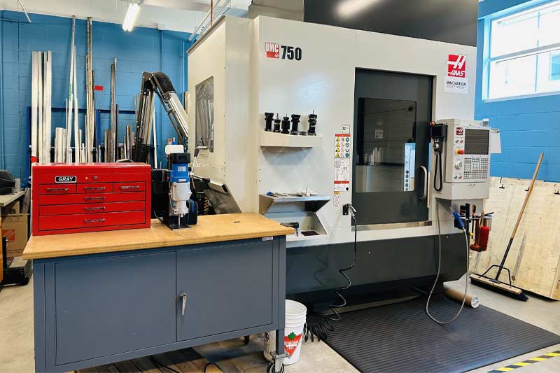 Atelier industriel avec une grande machine CNC Haas UMC 750, un plan de travail équipé et divers outils et matériaux, illustrant un environnement de production organisé et fonctionnel.