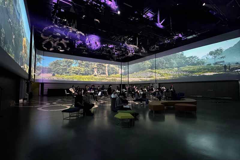 Grand espace intérieur moderne aménagé pour un atelier, avec des écrans panoramiques affichant des paysages naturels et des participants assis, créant un environnement immersif et interactif.