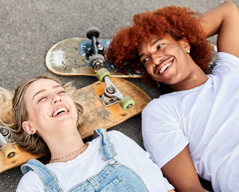 Two young people with skateboards lie on the floor and laugh together.