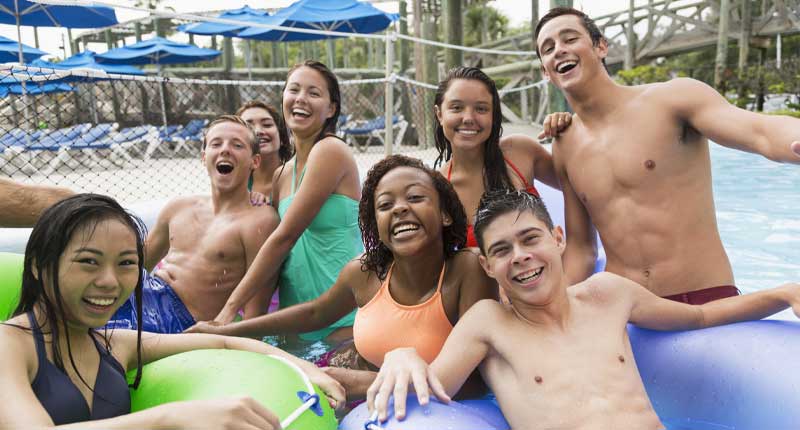 Un groupe d'adolescents d'horizons divers s'amuse ensemble dans un parc aquatique, riant et posant pour une photo en flottant sur l'eau. Ils semblent profiter d'une belle journée d'été au parc aquatique.