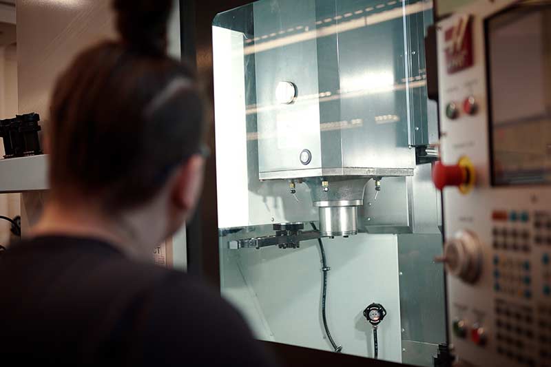 Personne observant une machine industrielle moderne dans un atelier ou une usine, mettant en avant la technologie, la précision et l’attention portée aux détails.