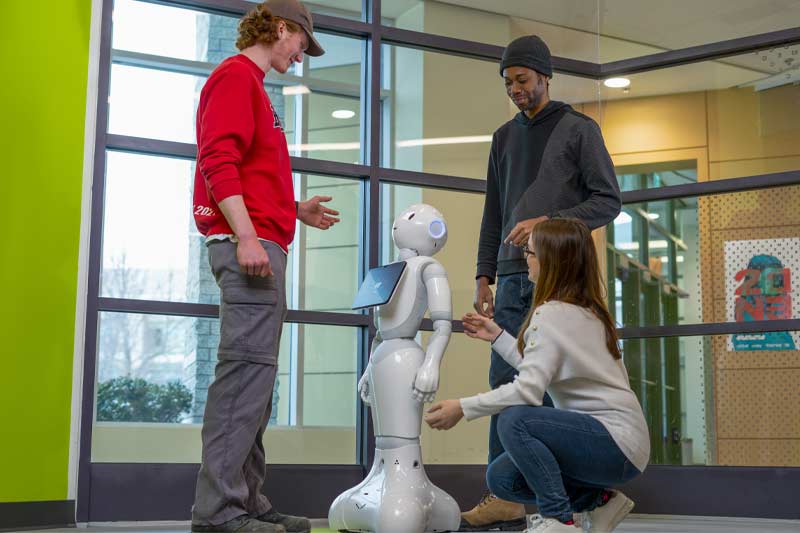 Groupe interagissant avec un robot humanoïde dans un laboratoire lumineux et moderne, illustrant collaboration, exploration et apprentissage technologique.