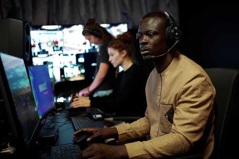 Studio ou salle de contrôle sombre, avec un homme portant un casque au premier plan et plusieurs personnes à des postes informatiques, supervisant du contenu numérique dans un environnement technique et concentré.