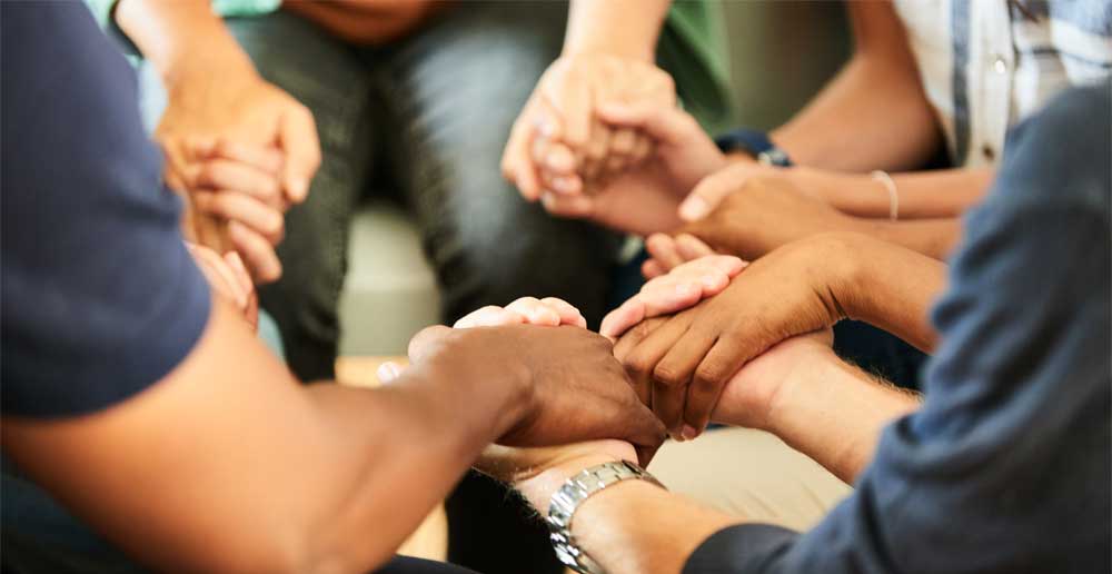 Gros plan d'un groupe de personnes diverses assises en cercle et se tenant la main lors d'une réunion d'un groupe de soutien