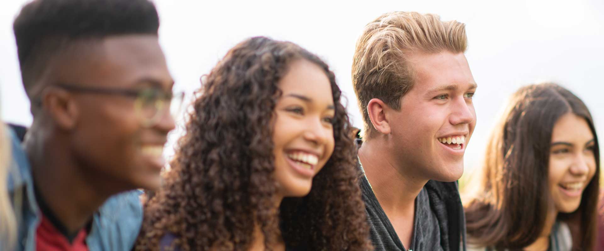 Quatre adolescents d'horizons différents sont assis sur des marches et sourient. Ils semblent apprécier leur compagnie mutuelle.